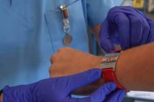 infirmiere avec des gants bleus vérifiant le bracelet d'un patient