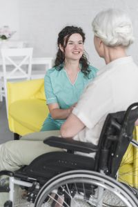 Infirmière souriante en soutien à une personne âgée assise sur un fauteuil roulant